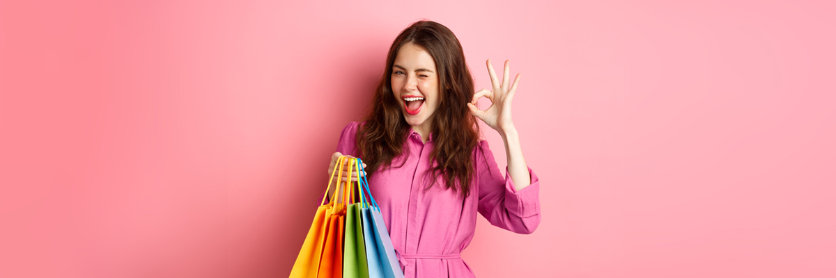 Young Happy Woman Shopper Showing Okay Sign, Winking Pleased With Good Discounts, Buying Staff On Sale, Holding Shopping Bags And Smiling Pleased, Pink Background